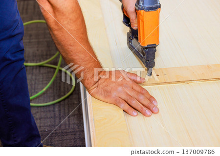 Carpenter is using air nail gun to attach wood piece on work surface in workshop. Carpenter is using air nail gun to attach wood piece on work surface in workshop. 137009786