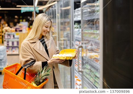 Woman choosing fresh eggs in supermarket refrigerator Woman choosing fresh eggs in supermarket refrigerator 137009896