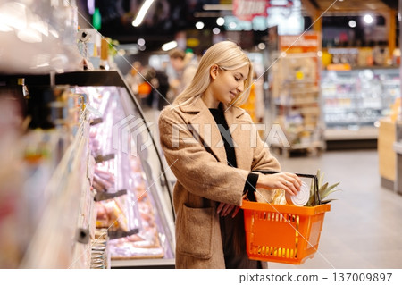 Woman choosing canned food, holding shopping basket in supermarket 137009897