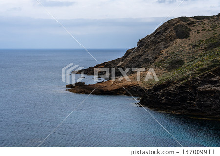 Coastal landscape of Menorca with cliffs meeting the sea under a cloudy sky. Coastal landscape of Menorca with cliffs meeting the sea under a cloudy sky. 137009911