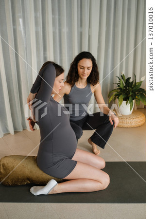 Pregnant woman practicing yoga with instructor in a bright room with curtains and plants during a daytime session focused on prenatal care 137010016