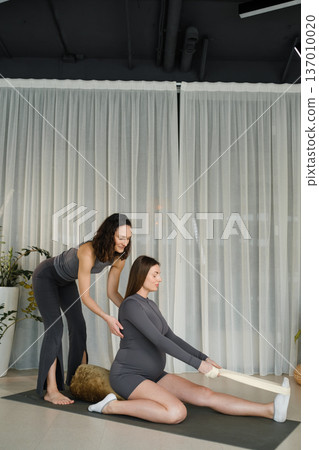 Pregnant woman stretches with instructor in modern studio during day Pregnant woman stretches with instructor in modern studio during day 137010020