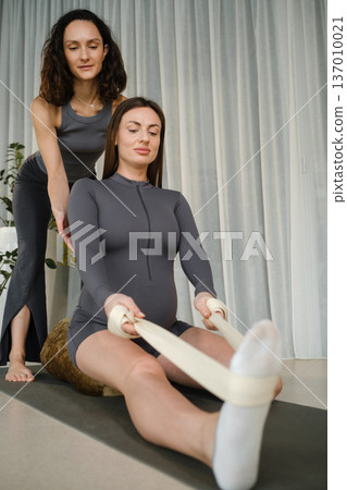 Two women practice stretching exercises in a bright studio during a workout session focused on flexibility and balance 137010021