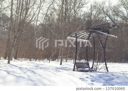 A handcrafted wrought iron garden swing, designed with an ornate frame and artistic top detailing, situated in a snowy outdoor setting. Outdoor A handcrafted wrought iron garden swing, designed with an ornate frame and artistic top detailing, situated in a snowy outdoor setting. Outdoor 137010060