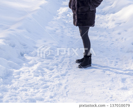 Woman wearing black ankle boots, walking on the snow. Season 137010079