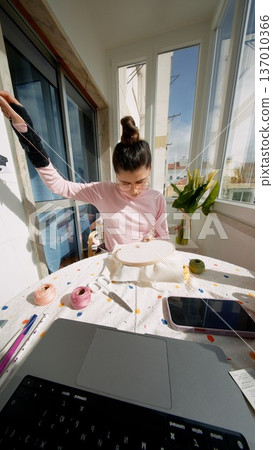 Young woman multitasking between laptop and embroidery 137010366