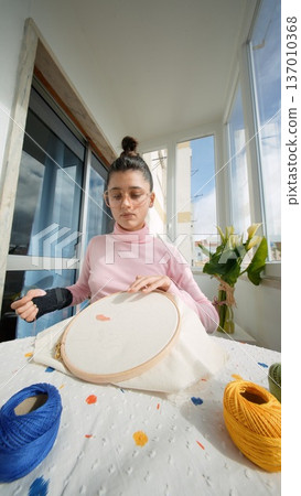 Woman stands proudly by window with vibrant embroidery on display Woman stands proudly by window with vibrant embroidery on display 137010368