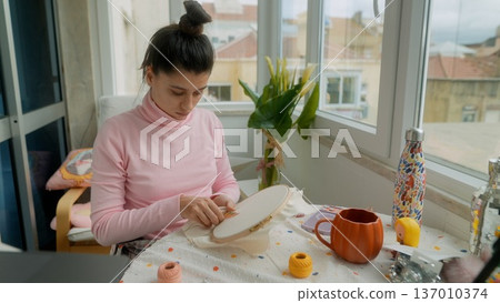 Focused woman crafting intricate embroidery under daylight 137010374