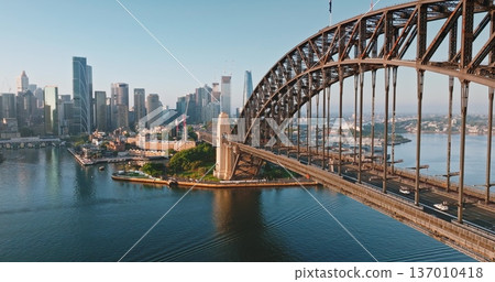 Australia, Sydney: Sydney Harbour Bridge and modern city skyline under sunny morning light, urban infrastructure architecture and road transportation traffic. Drone flight aerial panorama 137010418