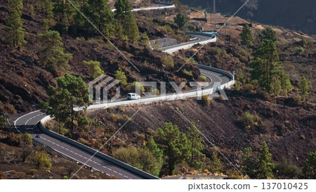 Tenerife, Canary Islands: Aerial view winding mountain road, with a van navigating curves among volcanic landscapes and lush pines green hills forest. Static shot Tenerife, Canary Islands: Aerial view winding mountain road, with a van navigating curves among volcanic landscapes and lush pines green hills forest. Static shot 137010425