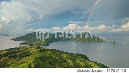 Vibrant rainbow arches Fiji islands with lush green mountains and coastal landscape meeting calm Pacific Ocean under bright sky. Perfect nature background. Travel destination. Aerial view drone flight Vibrant rainbow arches Fiji islands with lush green mountains and coastal landscape meeting calm Pacific Ocean under bright sky. Perfect nature background. Travel destination. Aerial view drone flight 137010426