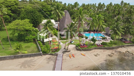 Tropical resort on Fiji Savusavu bay with palm-fringed sandy beach, pool and thatched bungalows under bright sky, kayaks at the waterfront for a luxury island getaway Tropical resort on Fiji Savusavu bay with palm-fringed sandy beach, pool and thatched bungalows under bright sky, kayaks at the waterfront for a luxury island getaway 137010456