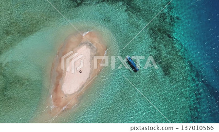 Tiny sandbar in turquoise waters of Lombok with traditional outrigger boat moored nearby, aerial drone view of pristine, tranquil tropical island escape perfect for snorkeling. Exotic nature, top down 137010566