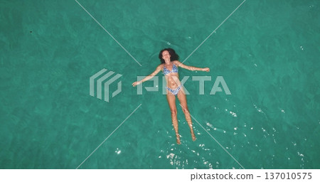 Young beautiful woman in bikini floats on her back in calm, transparent turquoise sea of Ko Lanta, feeling relaxed and enjoying peaceful summer vacation under the sun in Thailand. Top down aerial view Young beautiful woman in bikini floats on her back in calm, transparent turquoise sea of Ko Lanta, feeling relaxed and enjoying peaceful summer vacation under the sun in Thailand. Top down aerial view 137010575