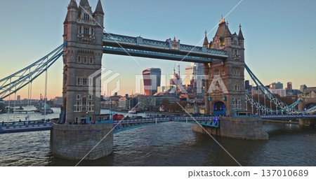 England, London: Tower Bridge standing majestically over River Thames with cityscape views, highlighting historic architecture and modern financial district against the evening sky. Panoramic footage 137010689