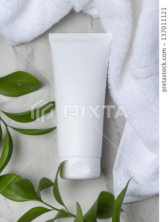 Mockup of blank white cream tube near white bath towel and green leaves. Unbranded cosmetic 137011121