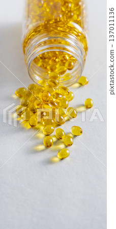 Yellow softgel scattered from transparent jar on greige ston, Nutritional supplements or vitamins 137011136