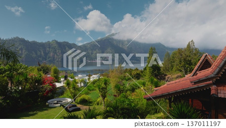 Balinese style traditional villa hotel resort with red roof tiles nestled in a lush tropical garden, offering stunning panoramic views of Lake Batur and Mount Abang in background. Aerial drone flight Balinese style traditional villa hotel resort with red roof tiles nestled in a lush tropical garden, offering stunning panoramic views of Lake Batur and Mount Abang in background. Aerial drone flight 137011197
