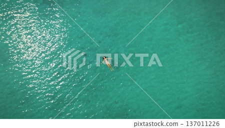 Young woman in bikini relaxing floating on back in crystal clear turquoise ocean water, enjoy serene summer holidays and vacation in tropical paradise. Aerial top down zoom out panorama drone flight 137011226