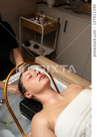 Young woman lying back, having a professional head spa and scalp treatment for hair health and deep relaxation Young woman lying back, having a professional head spa and scalp treatment for hair health and deep relaxation 137011349