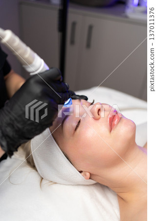 Woman undergoing a professional hydrafacial treatment for deep cleansing, exfoliation, and hydration at a modern aesthetic clinic 137011376
