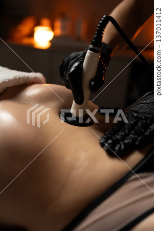 Professional performing radiofrequency body contouring on woman's abdomen for non-invasive skin tightening and rejuvenation, clinic setting 137011412