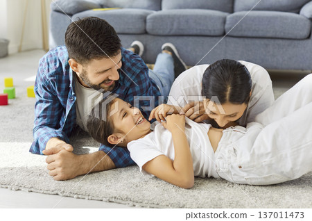 Happy parents and child laughing together at home, playful bonding on carpet 137011473