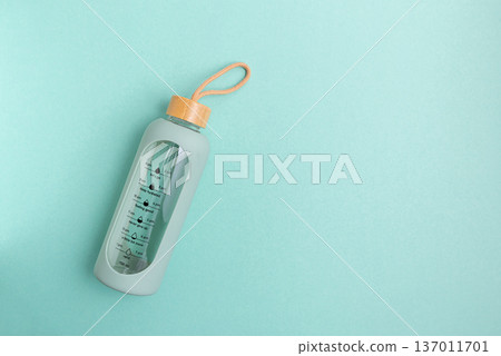 A glass water bottle with time markers on a blue background. 137011701