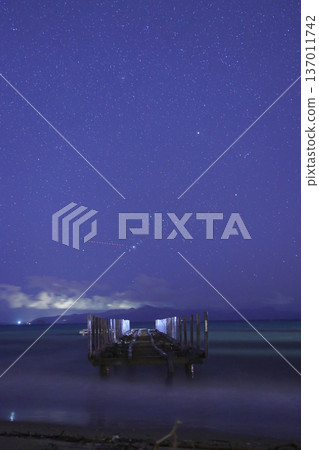A wrecked pier after a storm, and stars and clouds in the sky. Lightning and thunder over the islands in the Aegean Sea. A perfect photograph for a meteor shower. A wrecked pier after a storm, and stars and clouds in the sky. Lightning and thunder over the islands in the Aegean Sea. A perfect photograph for a meteor shower. 137011742