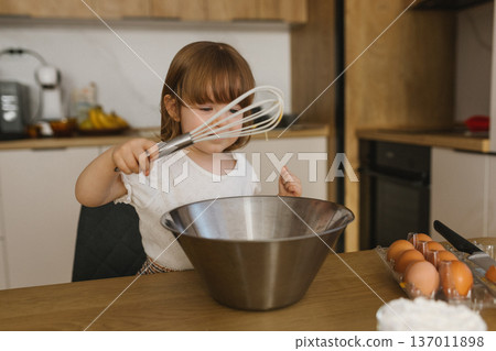 Little girl holding whisk over metal bowl in kitchen, child helping with baking at home, family lifestyle cooking scene Little girl holding whisk over metal bowl in kitchen, child helping with baking at home, family lifestyle cooking scene 137011898