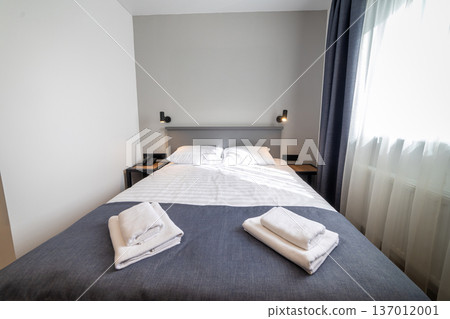 Cozy modern hotel bedroom with double bed fresh towels and soft natural window light 137012001