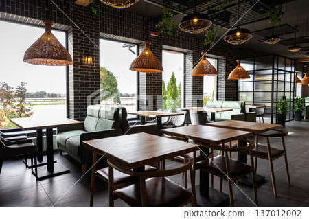 Modern restaurant interior with wooden tables and cozy seating near panoramic windows 137012002