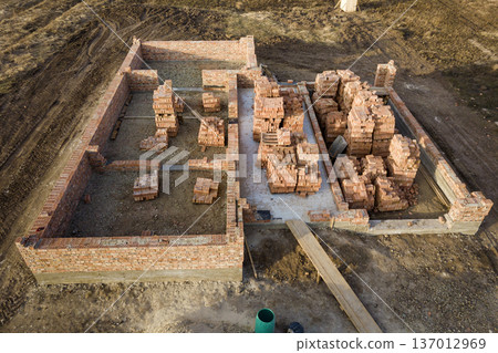 Aerial view of building site. Trenches dug in ground and filled with cement as foundation for future house, brick basement floor and stacks of brick for construction. 137012969