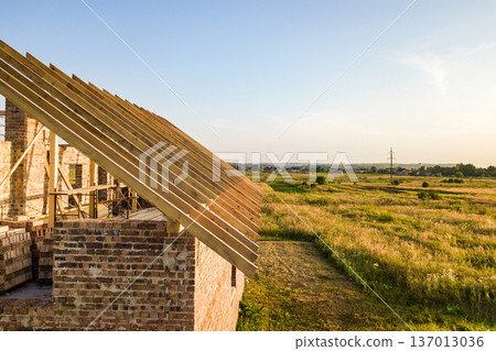 Unfinished brick house with wooden roof structure under construction. Unfinished brick house with wooden roof structure under construction. 137013036