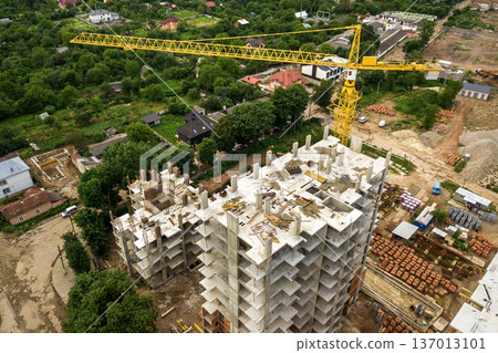 Aerial view of tower lifting crane and concrete frame of tall apartment residential buildings under construction in a city. Urban development and real estate growth concept. Aerial view of tower lifting crane and concrete frame of tall apartment residential buildings under construction in a city. Urban development and real estate growth concept. 137013101