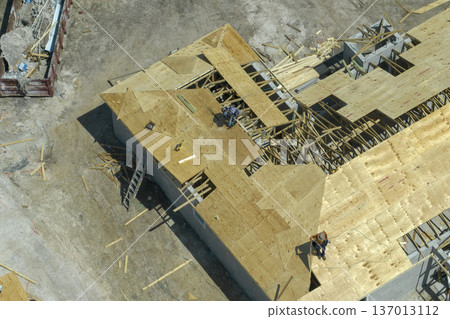 Aerial view of builders working on unfinished residential house with wooden roof frame structure under construction in Florida suburban area Aerial view of builders working on unfinished residential house with wooden roof frame structure under construction in Florida suburban area 137013112