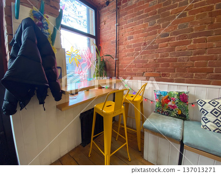 Cozy cafe corner with colorful pillows and wooden furniture. Relaxed social atmosphere, urban comfort, and creative interior design with eclectic details. 137013271