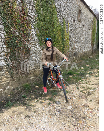 Woman riding bicycle near stone wall covered with ivy. Active lifestyle, outdoor recreation and countryside exploration concept Woman riding bicycle near stone wall covered with ivy. Active lifestyle, outdoor recreation and countryside exploration concept 137013306