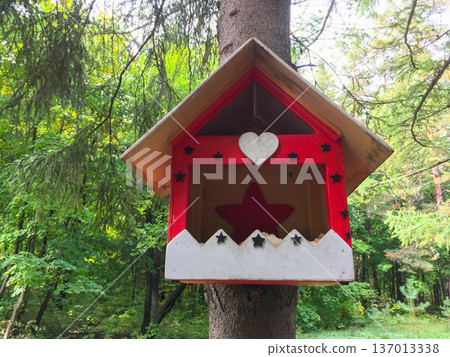 Red wooden birdhouse attached to tree in forest. Shelter, care for wildlife and environmental awareness concept 137013338