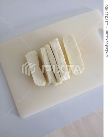 Sliced white halloumi cheese on cutting board in kitchen. Simplicity, nutrition, food preparation and home cooking routine Sliced white halloumi cheese on cutting board in kitchen. Simplicity, nutrition, food preparation and home cooking routine 137013400