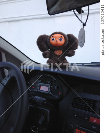 Plush toy Cheburashka placed on car dashboard inside vehicle. Travel companion, road trip adventure and mobility concept. Plush toy Cheburashka placed on car dashboard inside vehicle. Travel companion, road trip adventure and mobility concept. 137013411