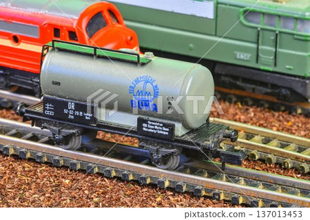 Detailed model of a vintage chemical tank car on a miniature railway track. A close-up view showcases a meticulously crafted model of a German DR tank positioned on a detailed model train track. 137013453