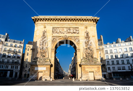 Scenic sunny view of the historic Porte Saint-Denis triumphal arch with intricate bas-relief carvings and classical Parisian buildings in Paris, France. 137013852
