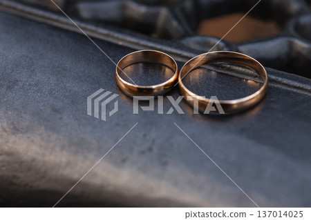 Two gold wedding rings lying on dark metal bench surface close up Two gold wedding rings lying on dark metal bench surface close up 137014025