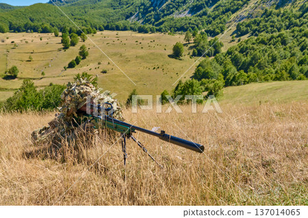 Soldier Sniper in Ghillie Suit Aiming Suppressed Sniper Rifle in Mountain Meadow During Training Soldier Sniper in Ghillie Suit Aiming Suppressed Sniper Rifle in Mountain Meadow During Training 137014065