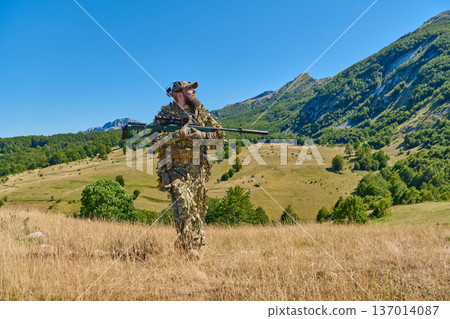 Camouflaged Sniper Soldier With Rifle Patrolling Mountain Meadow Under Clear Blue Sky 137014087