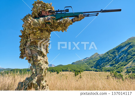 Sniper Soldier in Ghillie Camouflage Aiming High-Powered Rifle in Mountain Field Training 137014117