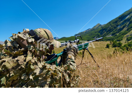 Camouflaged Sniper Soldier Lying Prone With Sniper Rifle In Mountain Field During Tactical Training Camouflaged Sniper Soldier Lying Prone With Sniper Rifle In Mountain Field During Tactical Training 137014125