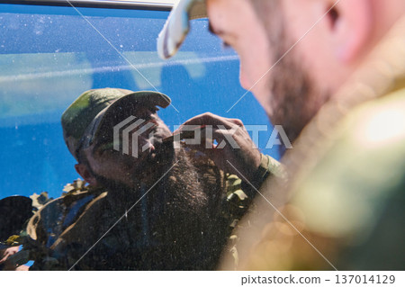 Soldier Applying Camouflage Face Paint in Mirror Preparing for Outdoor Mission or Hunt 137014129