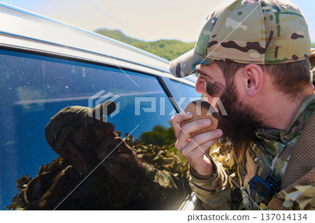 Soldier In Camouflage Cap Applying Face Paint While Looking At Vehicle Window Reflection Outdoors 137014134